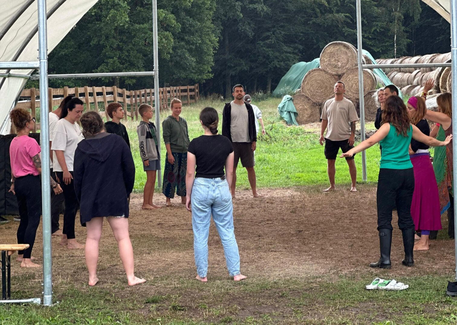 Siła wspólnoty i kręgu. Grupa uczestników warsztatów stoi w kręgu na świeżym powietrzu w Modlimowo Forest Camp, w tle bele słomy i las.