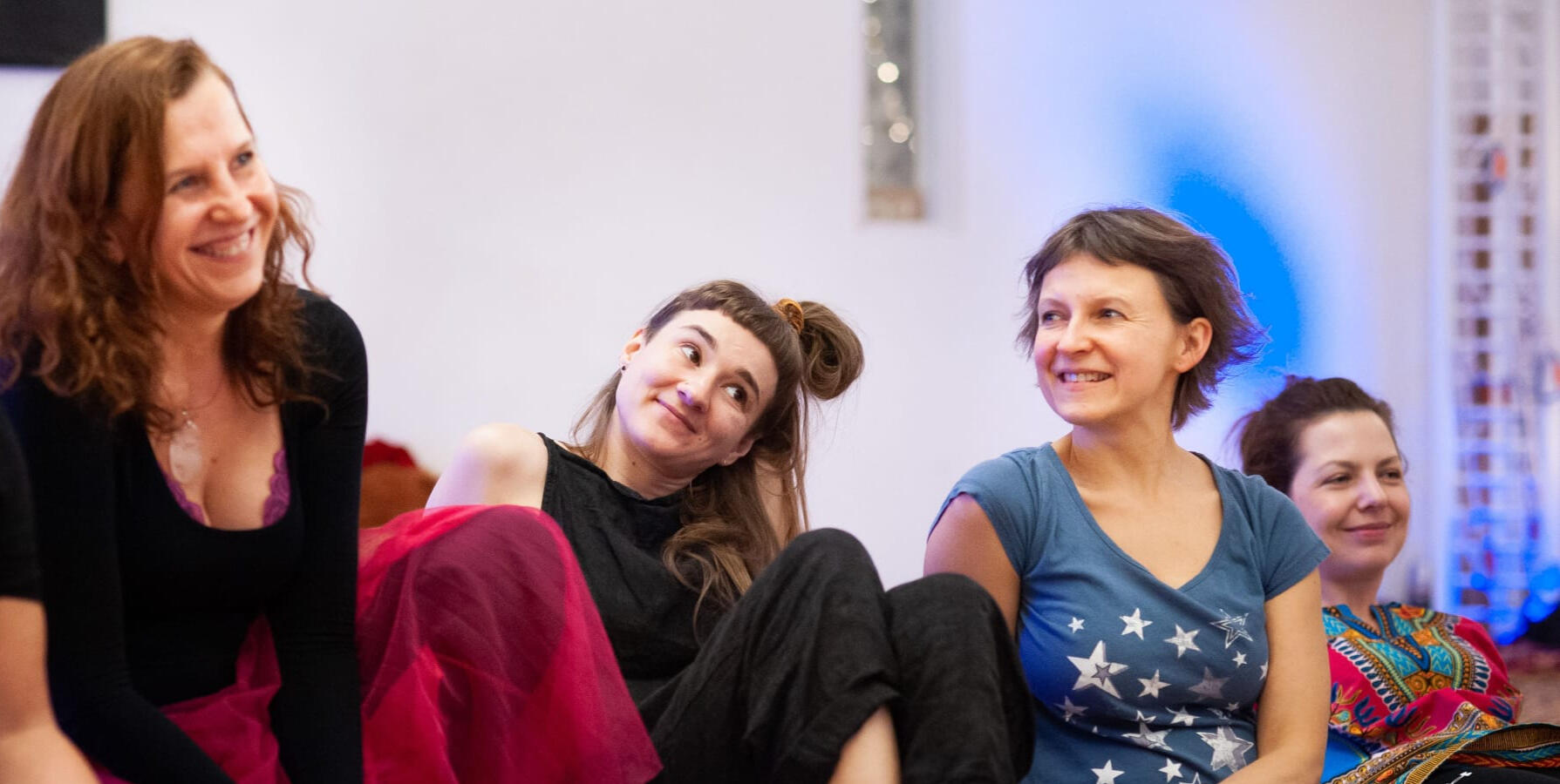 Trzy uśmiechnięte kobiety siedzące blisko siebie podczas warsztatów rozwojowych w nurcie mindfulness.