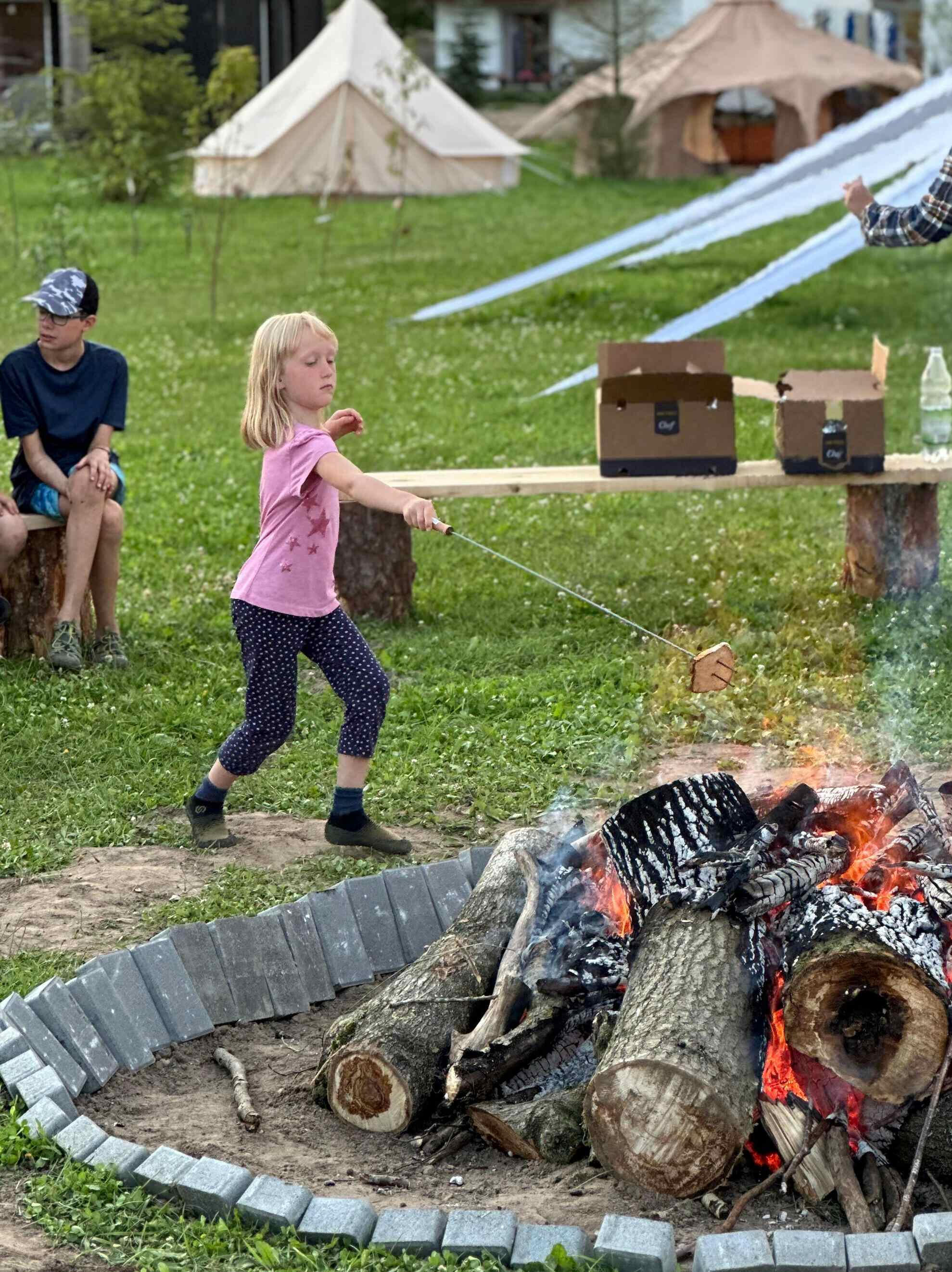 Dziewczynka w różowej koszulce piecze chleb nad ogniskiem podczas wieczornego spotkania w Modlimowie.