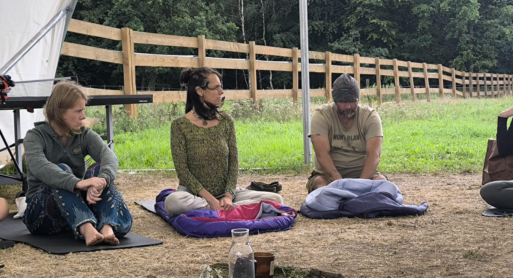 Uczestnicy siedzący na matach podczas sesji terapeutycznej na świeżym powietrzu, w tle drewniane ogrodzenie i las w Modlimowie.